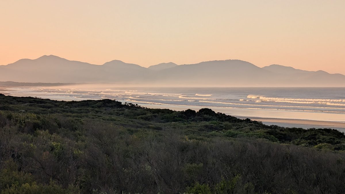 Coastal heath and a long surf beach at dawn, with the Wilsons Promontory ranges behind.